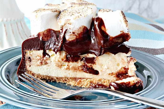 A slice of chocolate chip s'mores cheesecake on a blue plate with a fork.