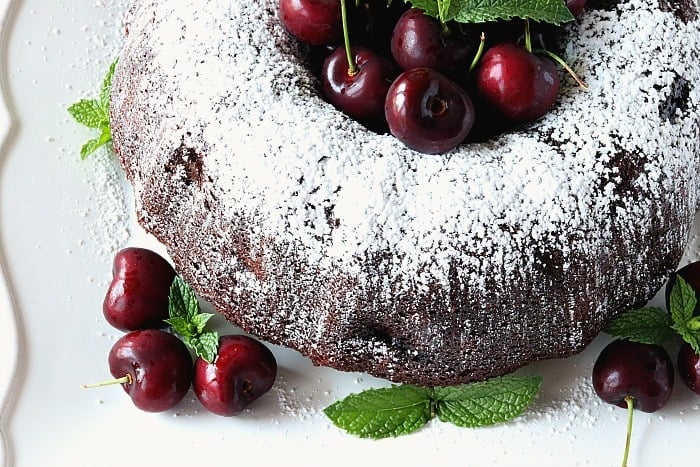 Overhead photo of half of a chocolate bundt cake with fresh cherries and mint garnish.