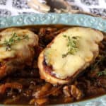 A pretty blue platter loaded with caramelized onions and topped with pork chops and melted cheese.