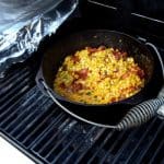 A cast iron pot of fried corn on an outdoor grill.