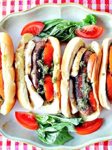 Four Caprese Sausage Sandwiches on a platter with tomatoes and fresh basil.