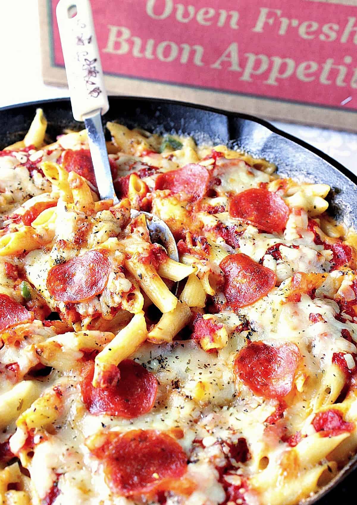 A cast iron skillet filled with Pizza Macaroni and Cheese topped with pepperoni.
