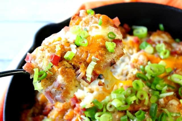 A closeup of a spoonful of tater tot poutine with cheese and green onion.