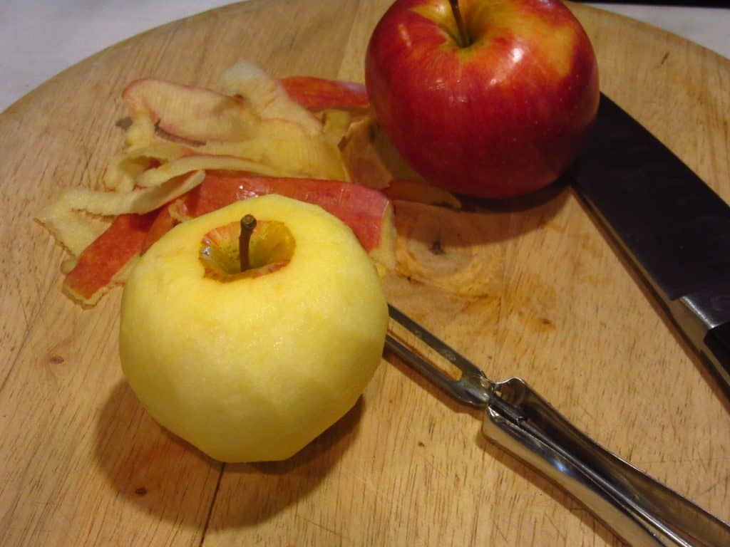 Two apples on a cutting board with a peeler.