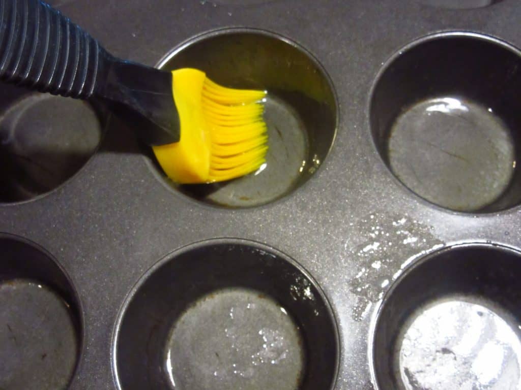 A pastry brush with melted butter in a muffin tin.