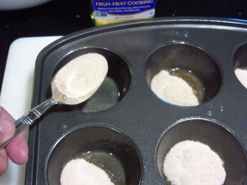 cinnamon sugar being spooned into muffin tins.