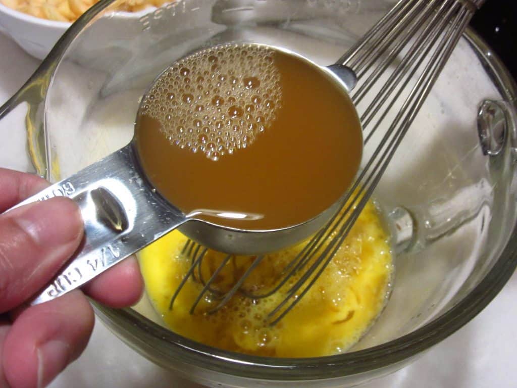 Apple juice being added to an egg in a bowl.
