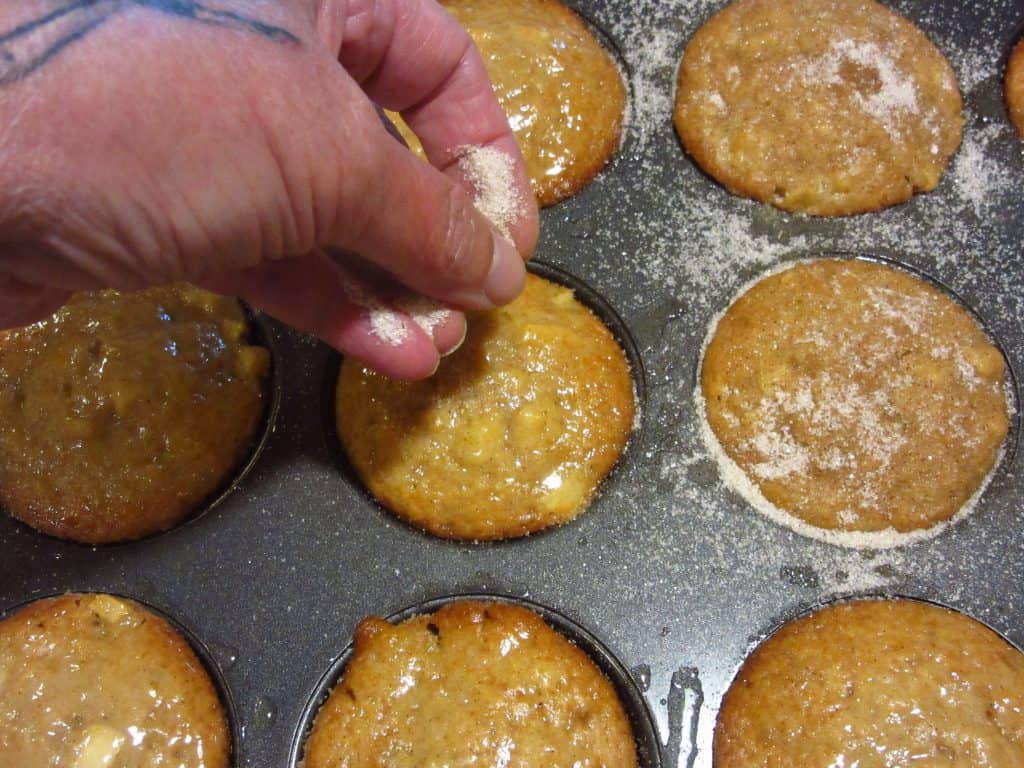 Cinnamon sugar being sprinkled over muffins.