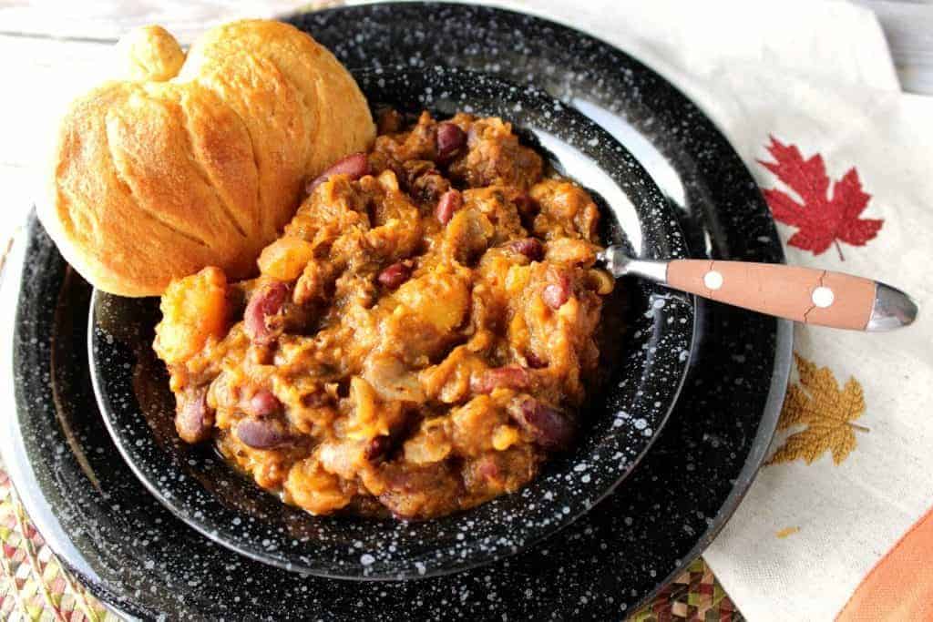 Overhead photo of a bowl of butternut squash chili with a pumpkin shaped biscuit.