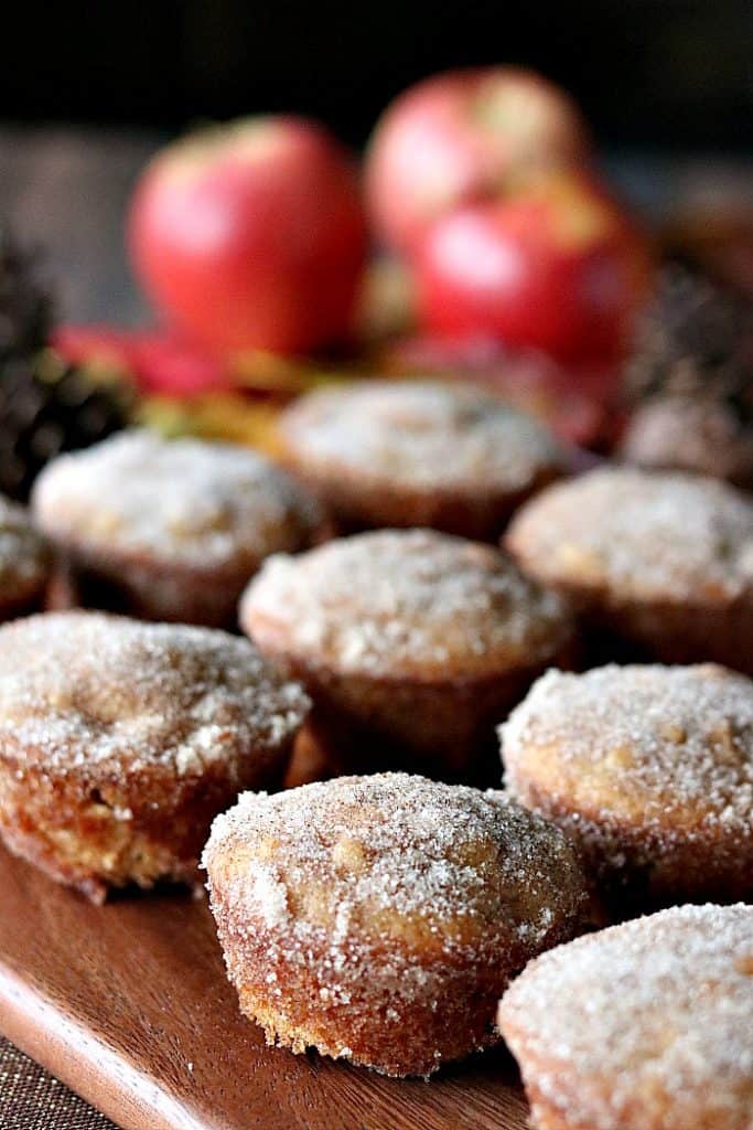 Vertical photo of apple cider donut muffins with cinnamon sugar coating and apples in the background.