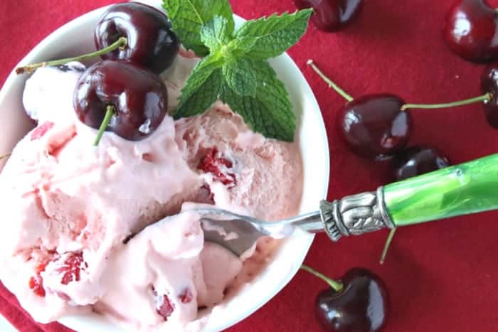 Offset photo of a dish of cherry chunk amaretto ice cream on a red tablecloth with a green spoon and a sprig of mint. Valentine's Day dinner recipe roundup.
