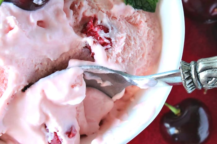 A closeup photo of a spoon in a dish of cherry chunk amaretto ice cream.