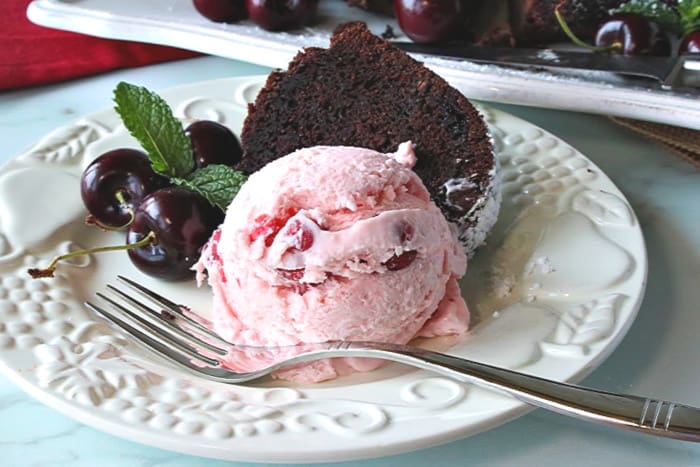 A scoop of cherry chunk amaretto ice cream on a plate with a slice of chocolate cake.