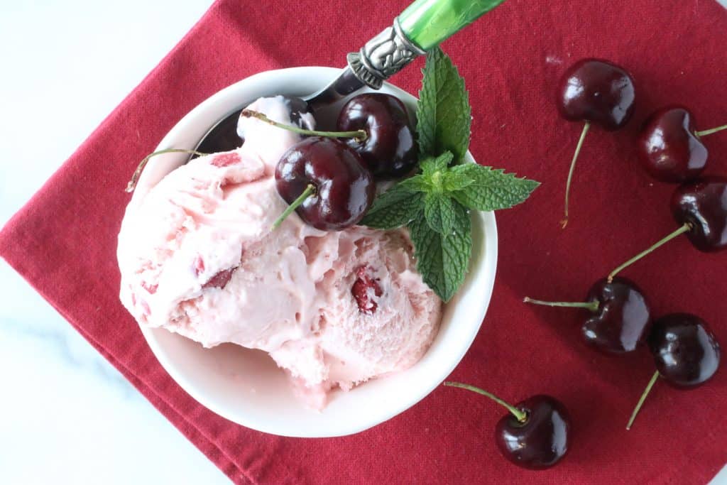 Overhead photo of a dish of cherry chunk amaretto ice cream with a spoon and mint sprigs.