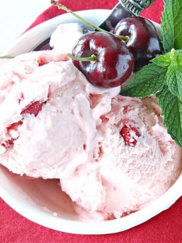 Scoops of No-Churn Cherry Chunk Amaretto Ice Cream in a bowl with cherries and mint.