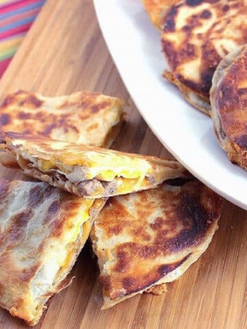 A Sausage and Egg Breakfast Quesadillas cut into quarters on a wooden board.