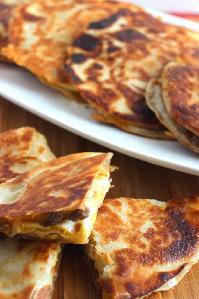 Closeup vertical photo of a breakfast quesadilla with sausage, egg, and cheese on a white platter.