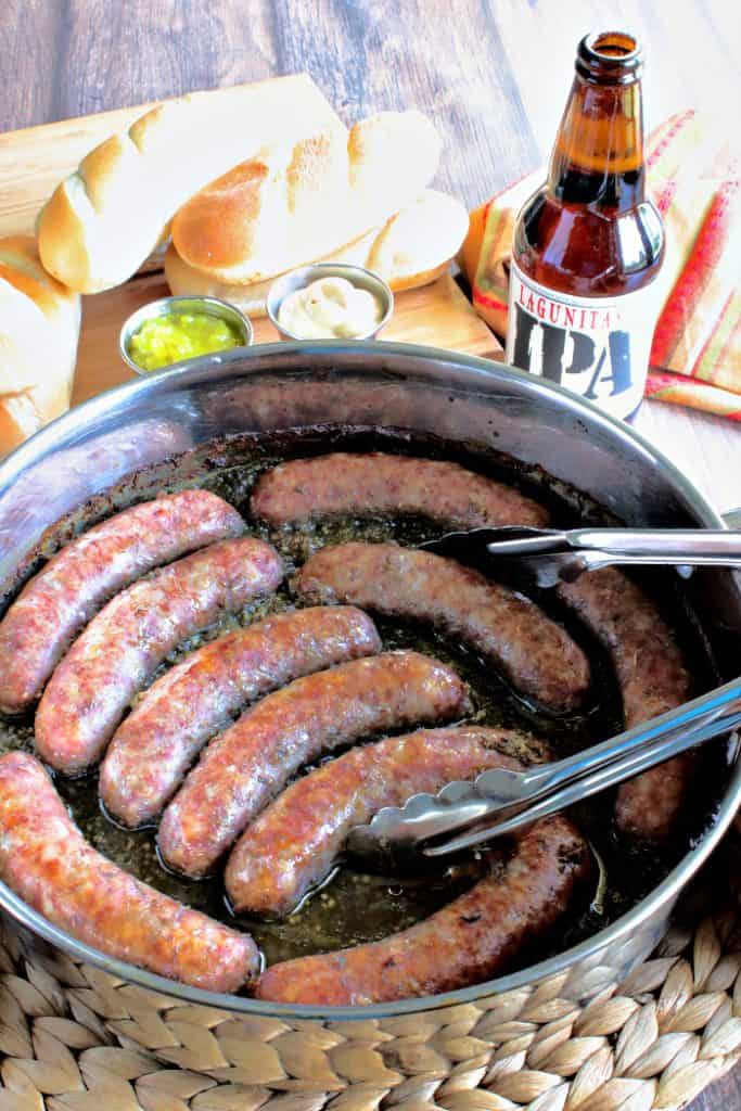 Overhead vertical photo of beer braised bratwurst in a skillet with buns and a bottle of beer in the background.