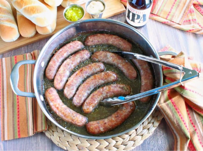 Overhead photo of a skilled filled with bratwurst in a beer and dill sauce. Buns and a bottle of beer are in the background.