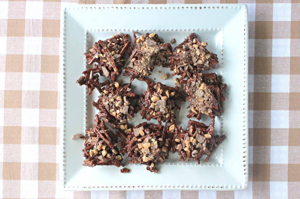 Overhead horizontal photo of a square white plate filled with chocolate covered shoestring haystacks with toffee bits.