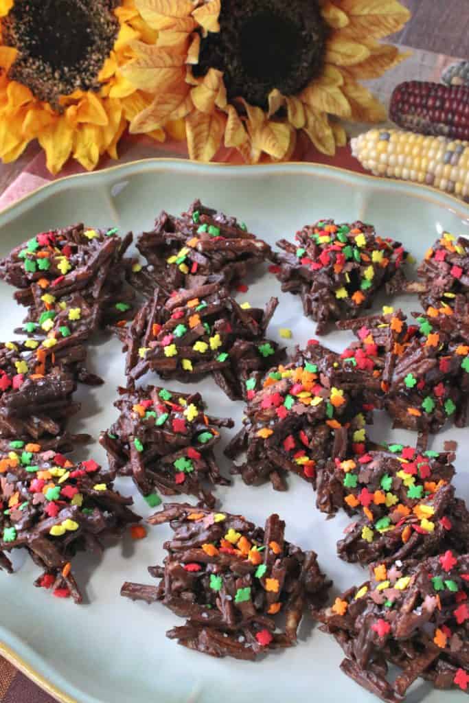A closeup vertical image of chocolate covered shoestring haystacks on a plate with sunflowers in the background.