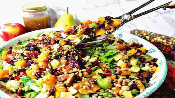 A closeup horizontal photo of salad tongs in a large bowl of colorful fall chopped salad
