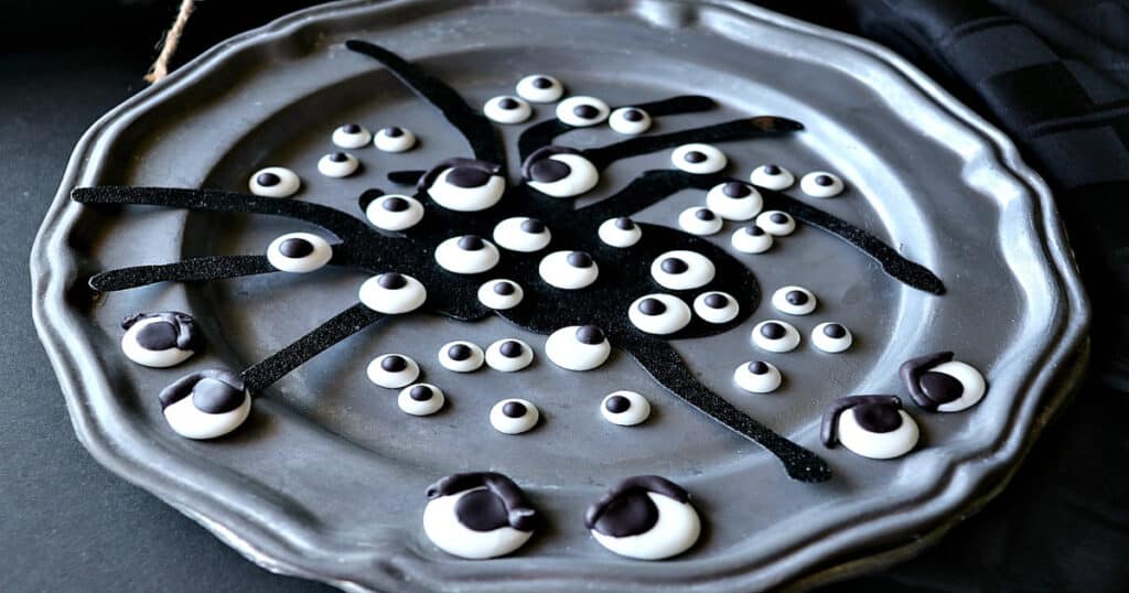 A pewter plate filled with Homemade Candy Eyeballs and a spider silhouette.