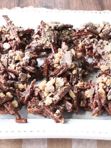 A plate filled with Chocolate Covered Shoestring Haystack cookies with toffee chips on top.