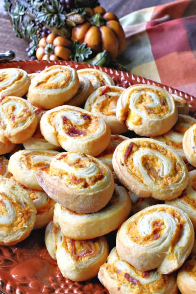 A orange platter piled high with pumpkin crescent pinwheel appetizers.