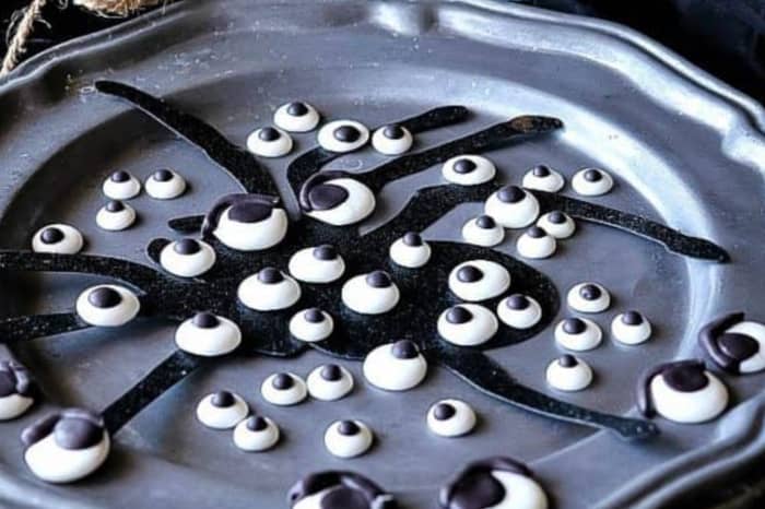 Closeup horizontal photo of royal icing eyeballs on a pewter plate with a spider silhouette.