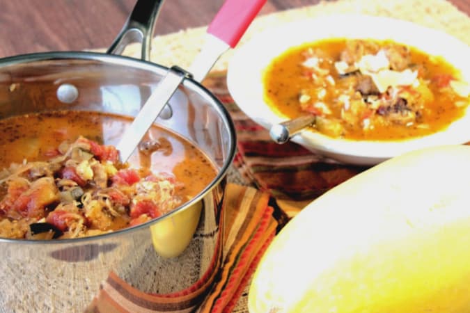 A pot of spaghetti squash soup with a ladle in the foreground and a bowl of spaghetti squash soup with a spoon in the background.