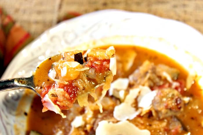 A closeup photo of a spoon with spaghetti squash soup with tomatoes, Parmesan cheese, and herbs.