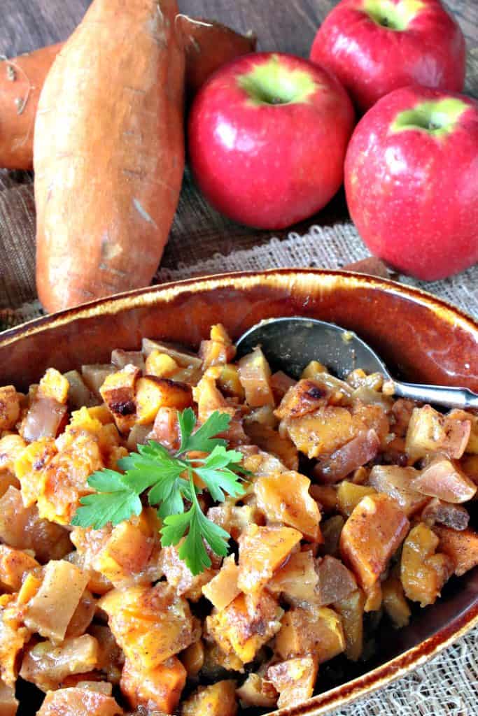 A vertical overhead photo of cinnamon sweet potatoes in a brown bowl with apples in the background