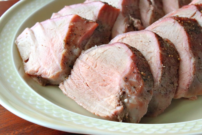 A horizontal photo of slices of slightly pink pork tenderloin on a plate.