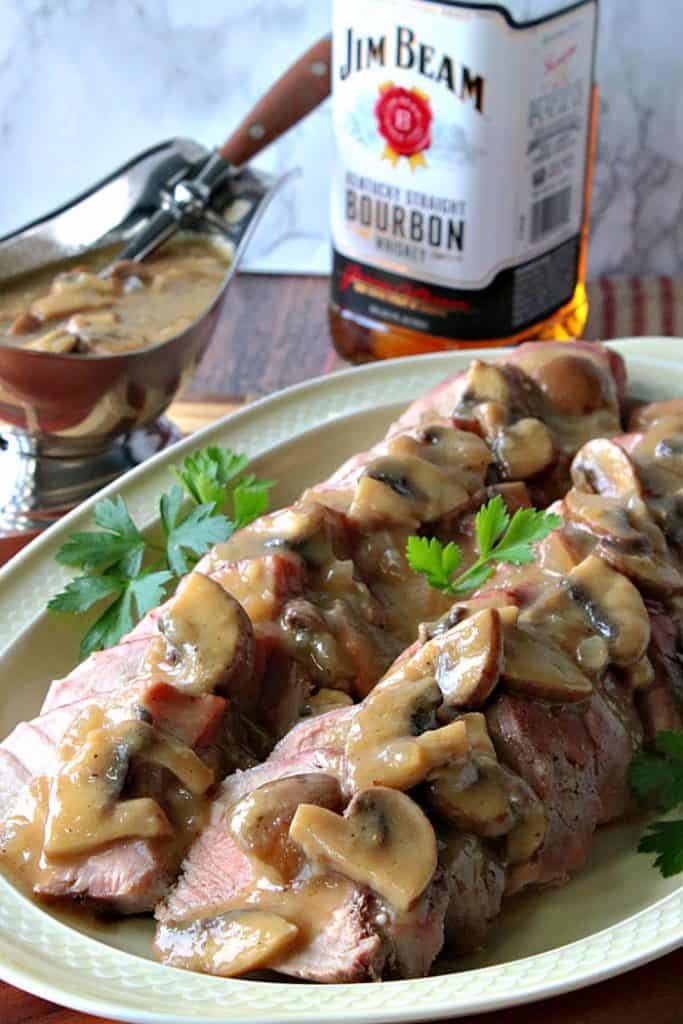Vertical photo of a sliced pork tenderloin on a plate smothered with mushroom gravy and garnished with parsley.