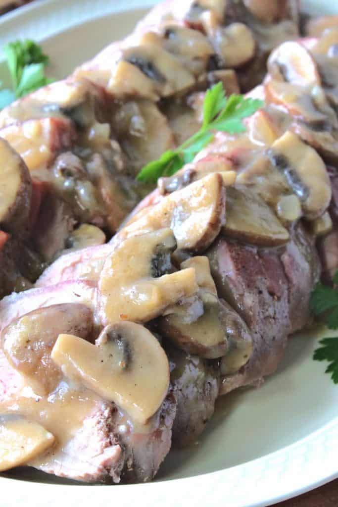 A vertical closeup image of slices of pork tenderloin smothered in mushroom bourbon gravy.