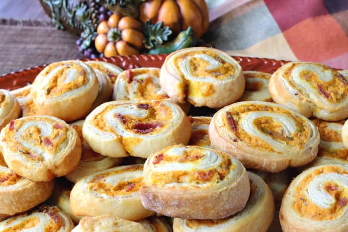 Closeup of a plate of crescent roll pinwheel appetizers filled with pumpkin, sage, and bacon.
