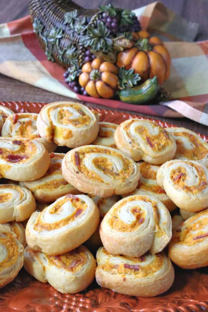 A vertical image of an orange plate filled with pumpkin sage pinwheel appetizers.