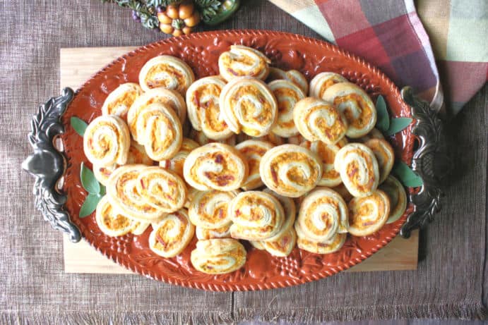 Overhead picture of an oval orange tray of savory pumpkin crescent pinwheel appetizers.