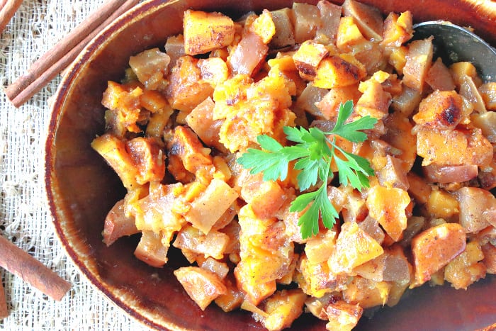 Overhead and offside photo of a bowl of cinnamon sweet potatoes and a sprig of parsley.