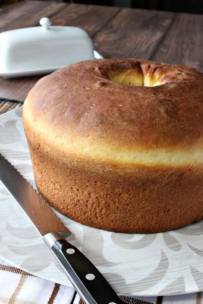Vertical closeup image of an entire loaf of Sally Lunn batter bread on a plate with a serrated knife.