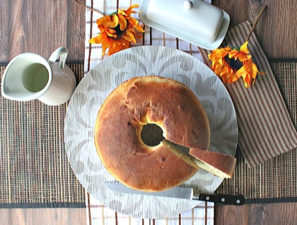 Overhead photo of a round loaf of Sally Lunn batter bread on a round plate with sunflowers and a butter dish.