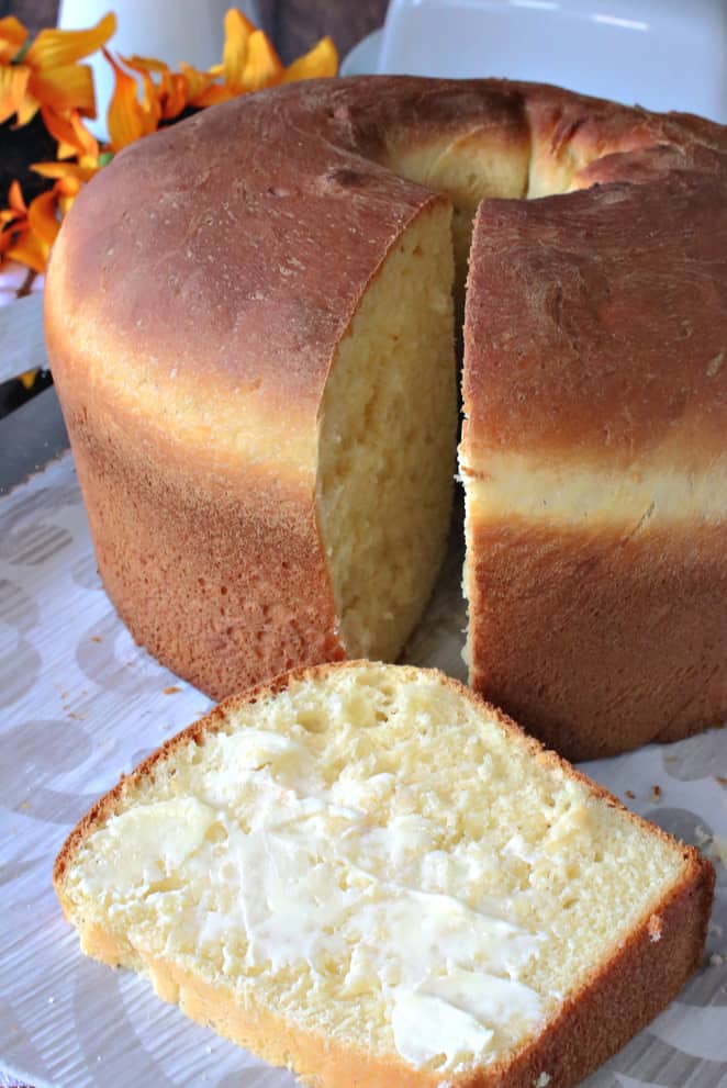 A vertical closeup picture of a slice of Sally Lunn enriched batter bread on a plate with butter.