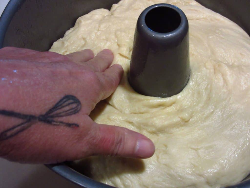 A hand smoothing out a batter bread in an angel food cake pan.