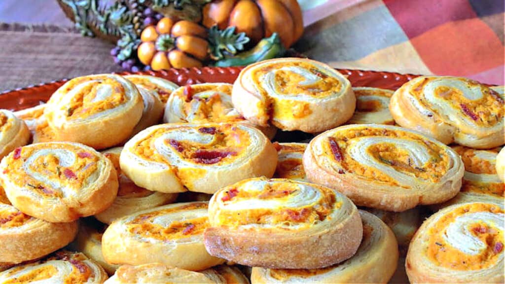 A pile of savory pumpkin pinwheel appetizers on a platter with a cornucopia in the background