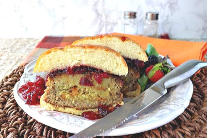 A turkey burger stuffed with stuffing cut in half on a plate with a knife of the side.