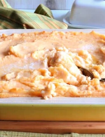 A horizontal photo of a yellow casserole dish of cheesy horseradish mashed potatoes casserole with a spoon.