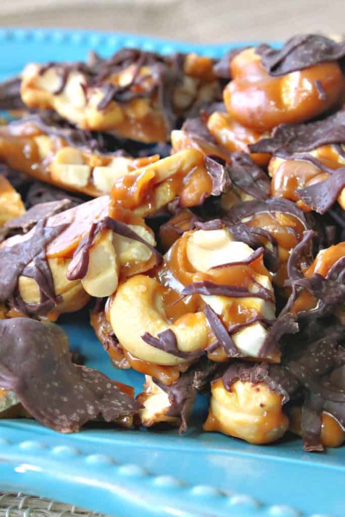  A closeup vertical photo of toffee cashew clusters on a blue plate.