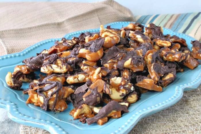 A blue plate fulled with butter toffee cashew clusters with chocolate.