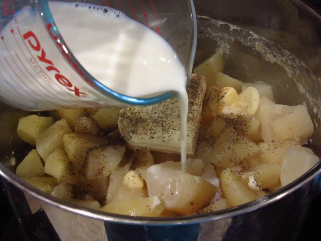 Milk being added to a pot of mashed potatoes.